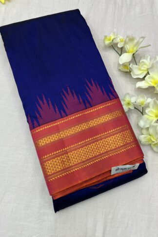 Ilkal Pure Silk Saree in royal blue and magenta with intricate golden zari border, placed beside white flowers on a soft fabric background