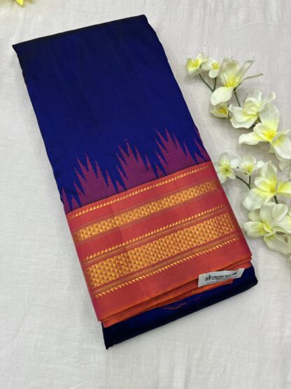 Ilkal Pure Silk Saree in royal blue and magenta with intricate golden zari border, placed beside white flowers on a soft fabric background